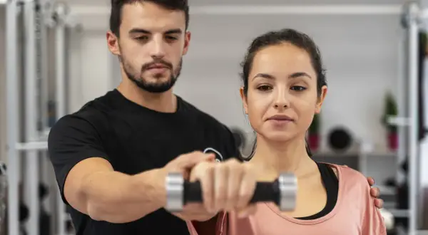 Trener pomaga kobiecie podnosić hantle podczas treningu CrossFit.