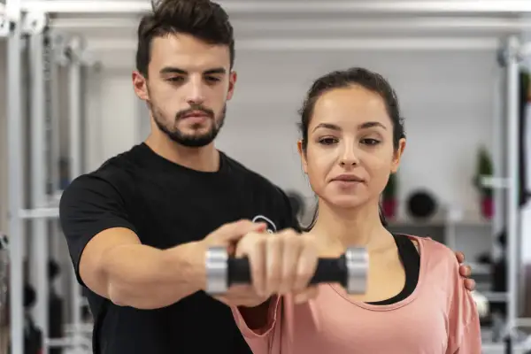 Trener pomaga kobiecie podnosić hantle podczas treningu CrossFit.